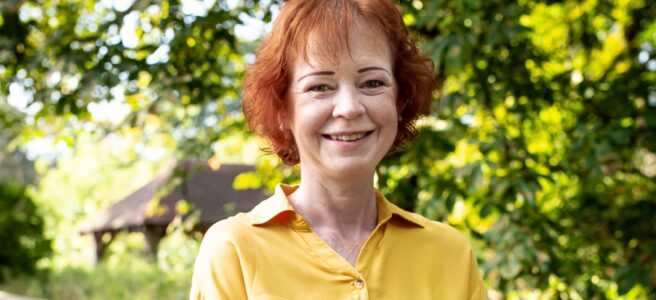 Photo of Joan Faria wearing yellow blouse, trees in background